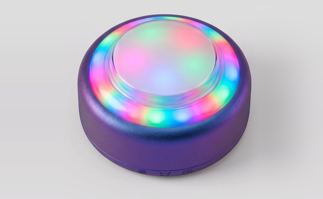 Puck, a round purple device with one big dome button on top, its ring of lights glowing in rainbow colors.